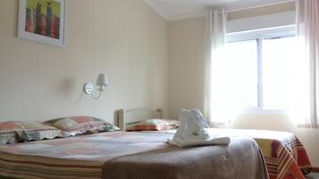 A hotel room with a bed, a nightstand, a wall-mounted lamp, a window with curtains, and a painting on the wall.