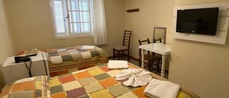 Habitación de hotel con dos camas, televisión, escritorio y ventana con cortinas.