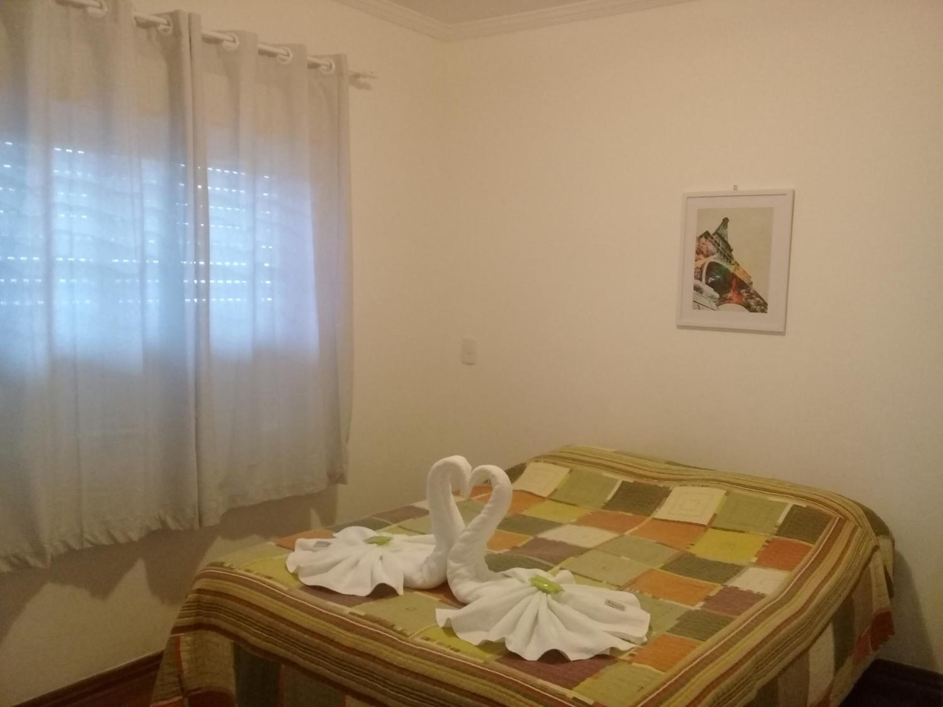 Een kamer met een bed, een raam met gordijnen en een ingelijste foto aan de muur.