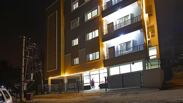 A multi-story building with illuminated windows and balconies, a gated entrance, and a visible parking area. - Tranzotel Bangalore Airport Hotel (Bengaluru)