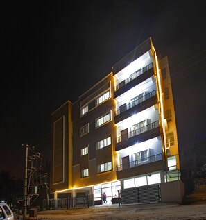 A multi-story building with illuminated windows and balconies, a gated entrance, and a visible parking area. - Tranzotel Bangalore Airport Hotel (Bengaluru)