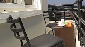A balcony with a chair, a small table, and a window with a view of the city. - Tranzotel Bangalore Airport Hotel (Bengaluru)