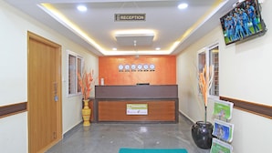A reception area with a wooden reception desk, a reception sign, a clock, and a TV mounted on the wall. - Tranzotel Bangalore Airport Hotel (Bengaluru)