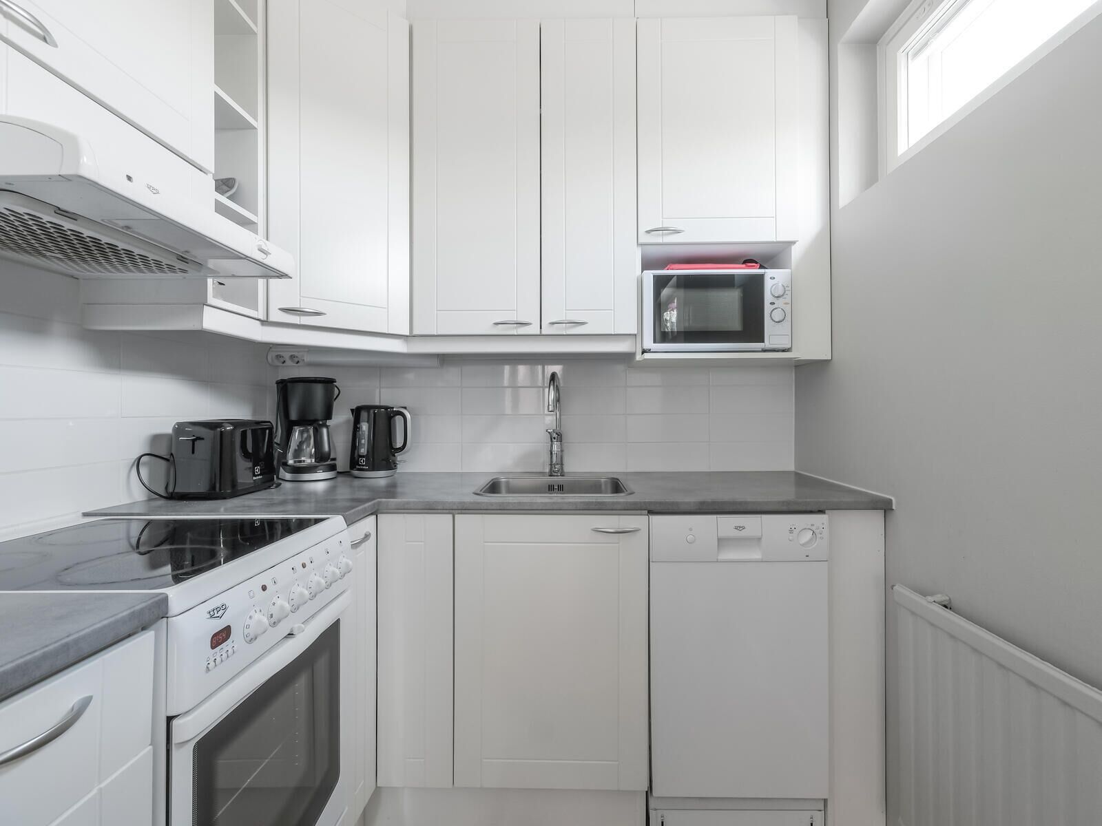 A compact kitchen with white cabinetry, a built-in microwave, a coffee maker, a toaster, and a dishwasher.