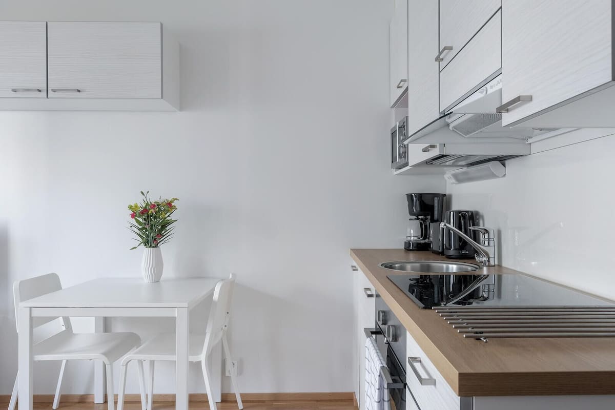 A modern kitchen with white cabinetry, a wooden countertop, and a dining area with white chairs and a vase of flowers.