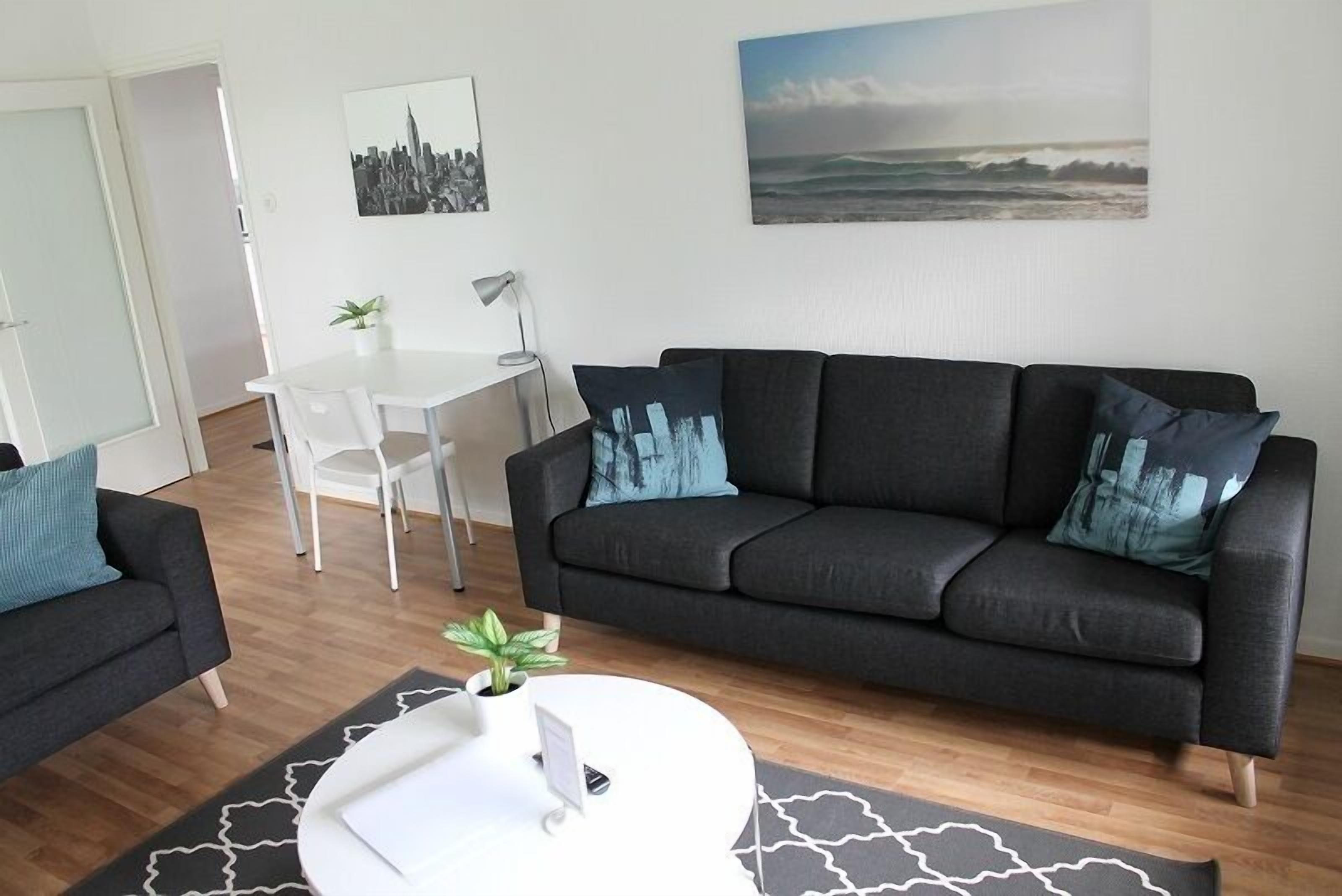 A modern living room with a dark grey sofa, a white coffee table, and a cityscape painting on the wall.
