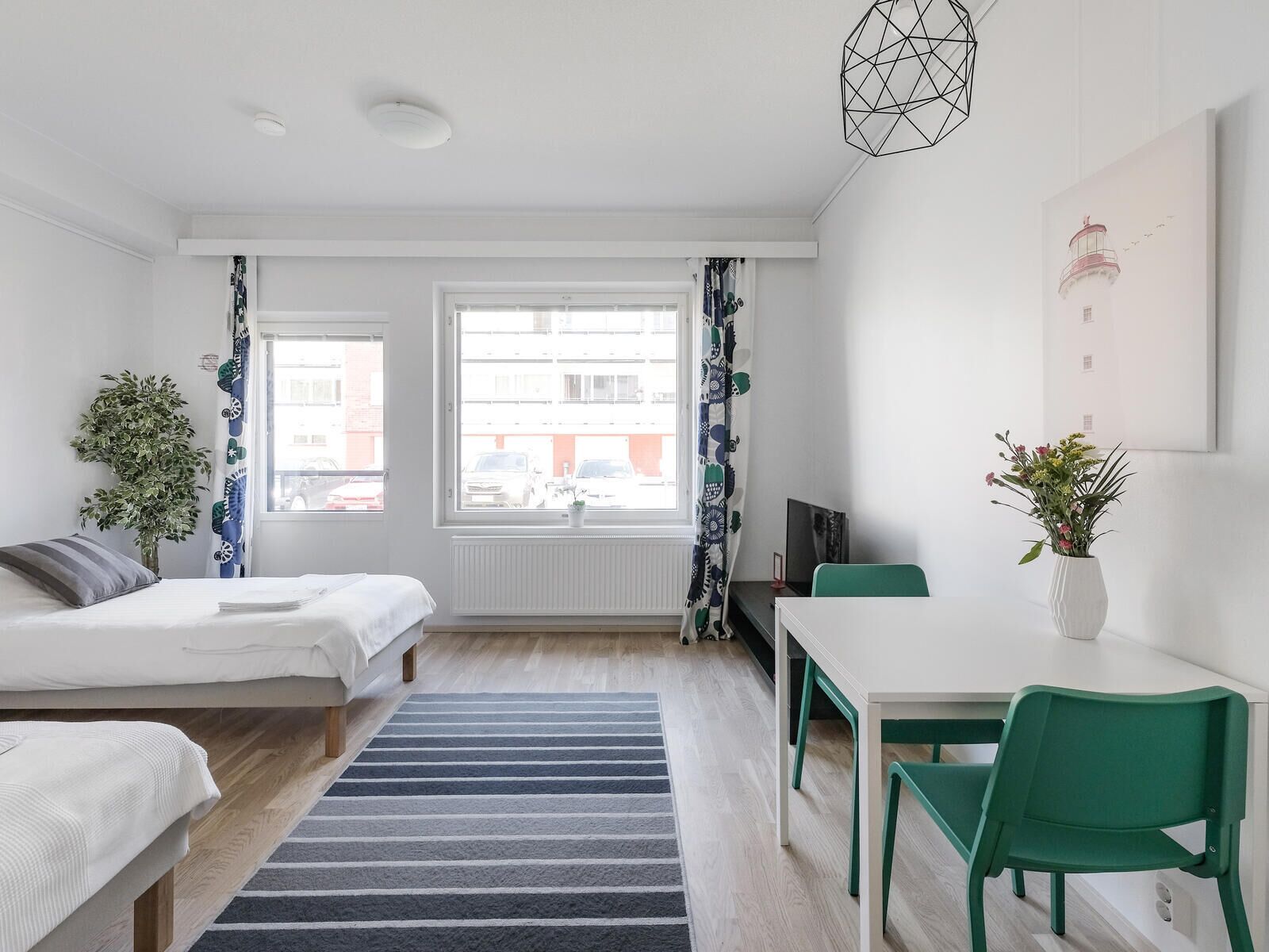 A modern, well-lit bedroom with a bed, a desk, and a chair, a large window with curtains, and a potted plant.