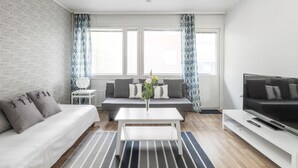 Un salon moderne comprenant un canapé, une table basse, un téléviseur et un coin salon avec des coussins.
