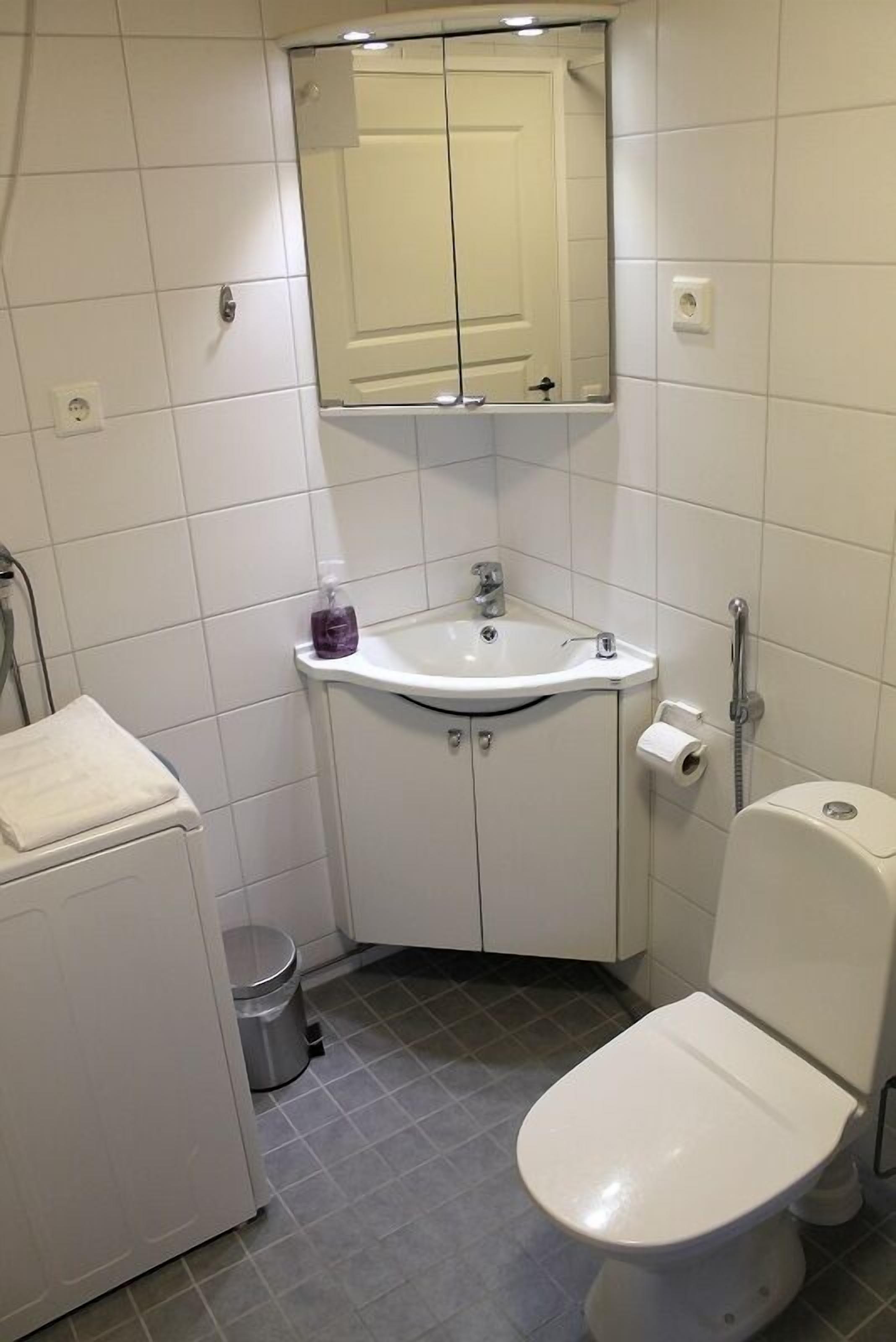 Une petite salle de bain compacte avec un lavabo blanc, des toilettes et un miroir au-dessus du lavabo.
