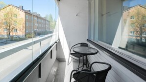 Un balcon donnant sur une rue et des immeubles. On y trouve deux chaises et une petite table.