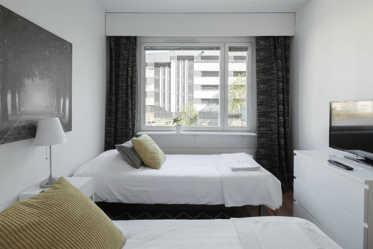 A hotel room with a bed, a desk with a TV, a window with curtains, and a painting on the wall.
