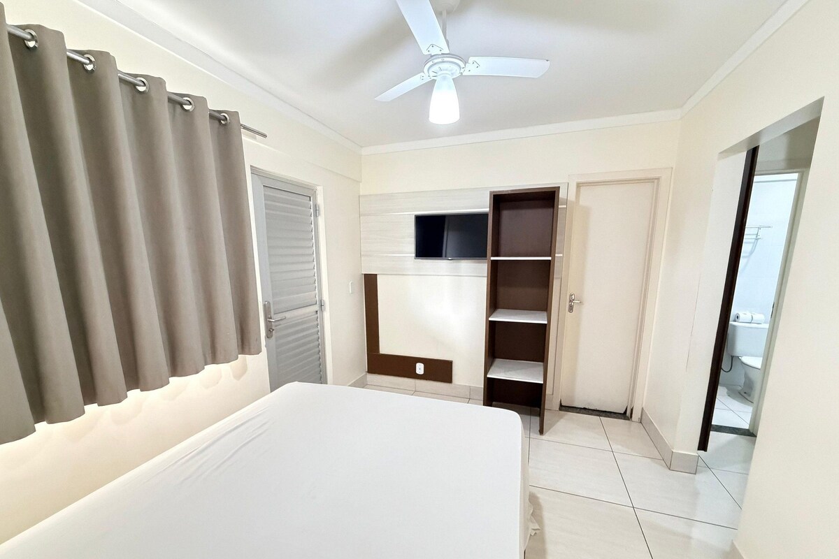 Un dormitorio con cama, armario, televisor y ventilador de techo.