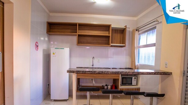 Cocina compacta con refrigerador, microondas y armarios de madera. Hay tres taburetes de bar y una ventana que proporciona luz natural.