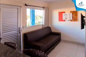 A living room with a sofa, a window, a wall-mounted sign, and a door. - Lacqua DiRoma V Via Caldas (Caldas Novas)