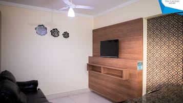 Uma sala de estar com sofá, televisão na parede, ventilador de teto e arte decorativa.