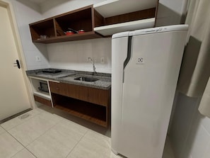 Una cocina con encimera de granito, pileta integrada, estantes de madera y refrigerador blanco.