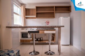 Una cocina con encimera de granito, dos taburetes de bar, un microondas y un refrigerador blanco.