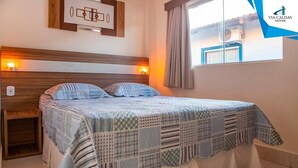 Un dormitorio con cama, mesitas de noche, una obra de arte en la pared, una ventana con cortinas y un logotipo visible.