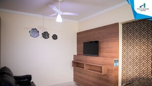 Una sala de estar con un sofá, un televisor montado, un ventilador de techo y detalles decorativos en la pared.