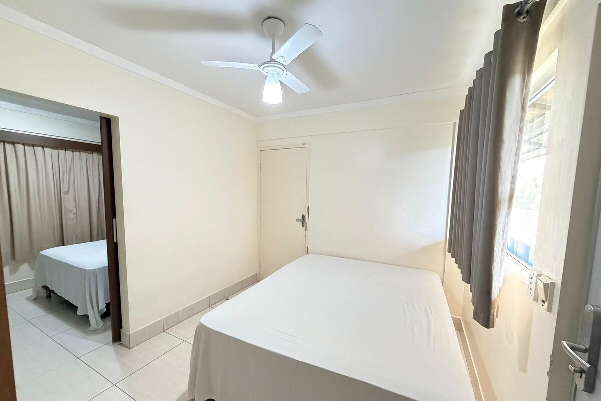 Una habitación de hotel con una cama individual, ventilador de techo, una puerta y una ventana con cortinas.