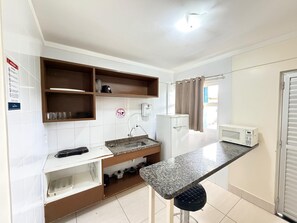 Una cocina compacta con lavamanos, encimera, microondas y un refrigerador pequeño.