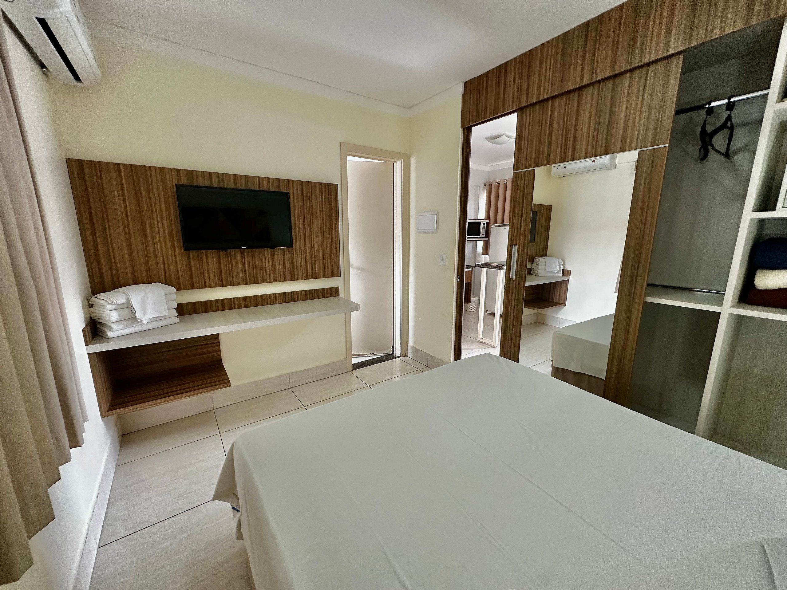 A hotel room with a bed, a TV mounted on the wall, a wardrobe, and a small kitchenette.