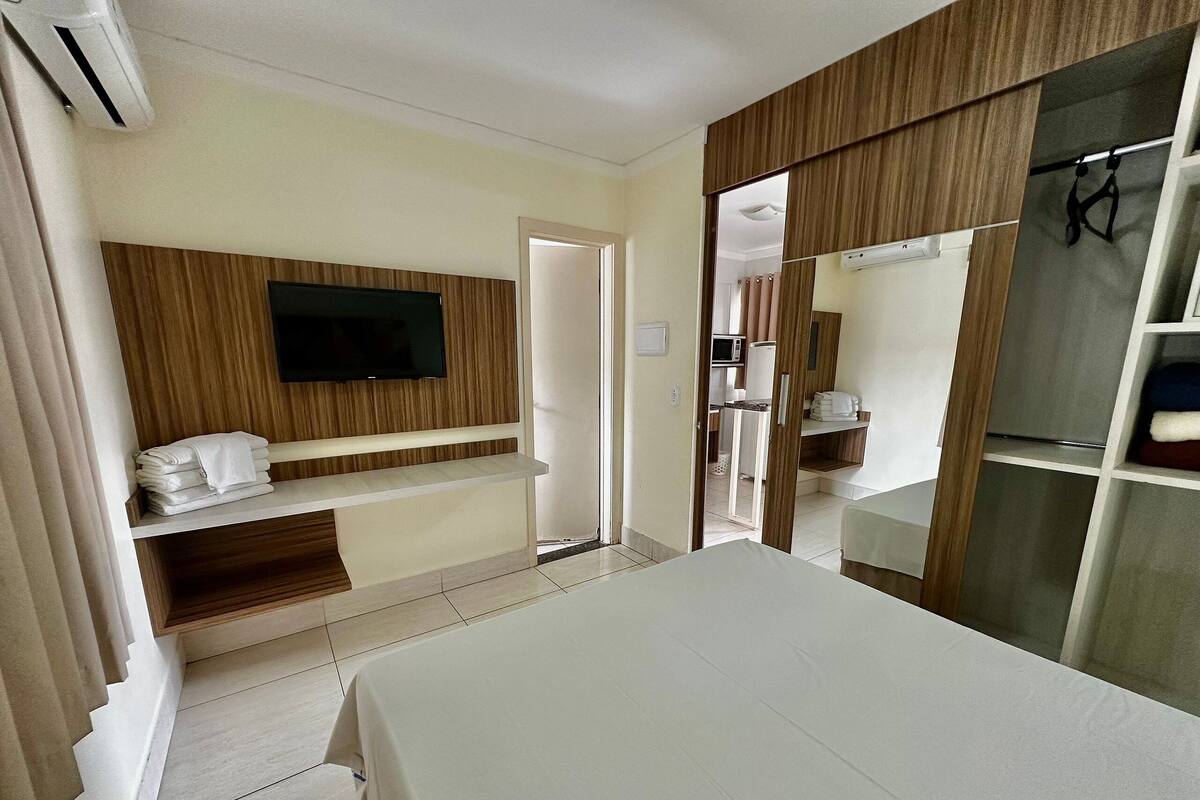 Hotellihuone, jossa on sänky, seinälle asennettu televisio, vaatekaappi ja pieni keittonurkkaus.