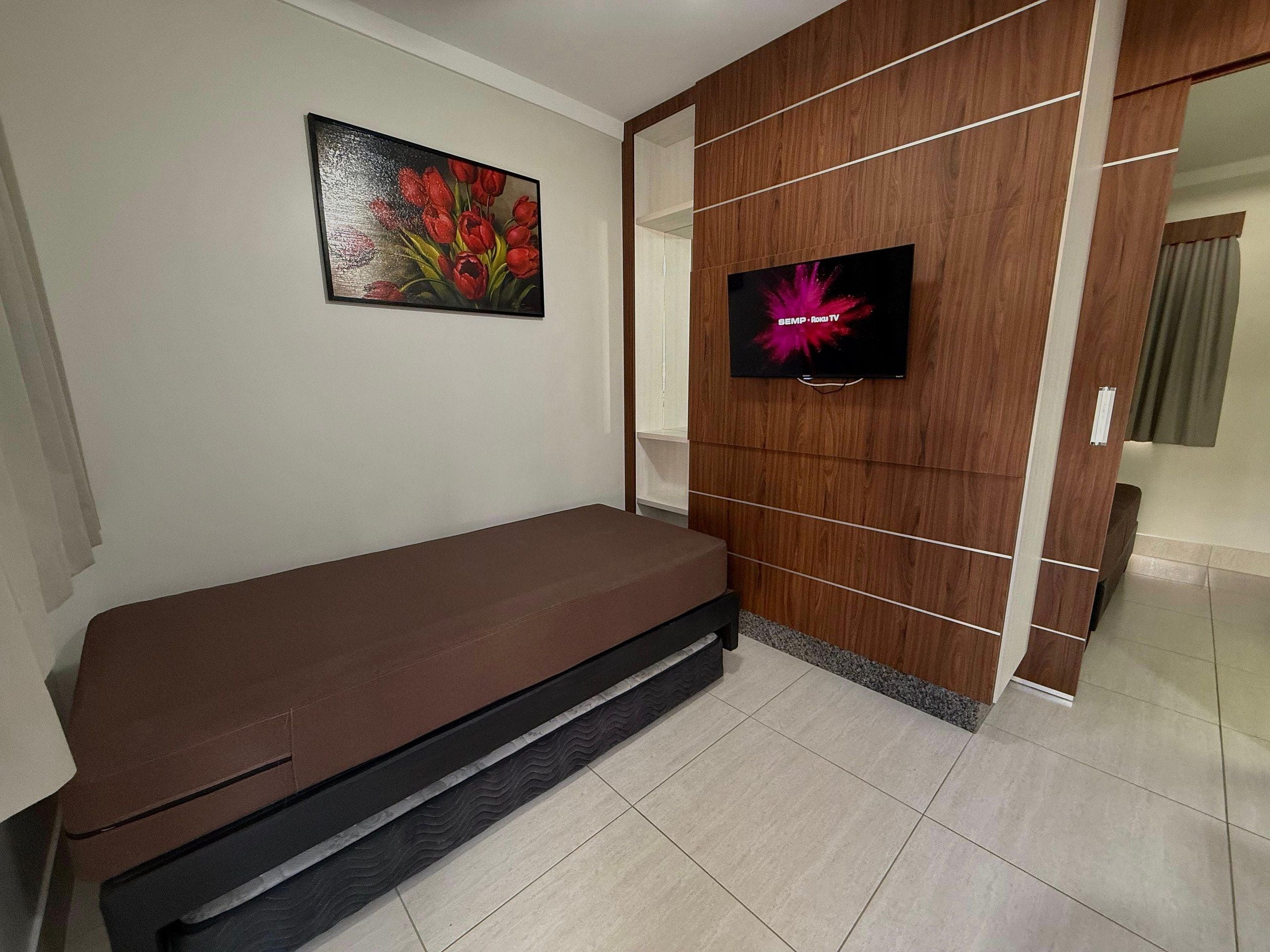 Quarto com sofá marrom, televisão na parede e pintura floral.