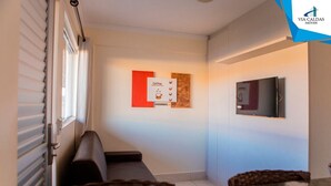 A hallway with a sofa, a TV mounted on the wall, and a bulletin board with a coffee advertisement. - Lacqua DiRoma V Via Caldas (Caldas Novas)