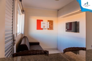 A hallway with a sofa, a TV mounted on the wall, and a bulletin board with a coffee advertisement. - Lacqua DiRoma V Via Caldas (Caldas Novas)