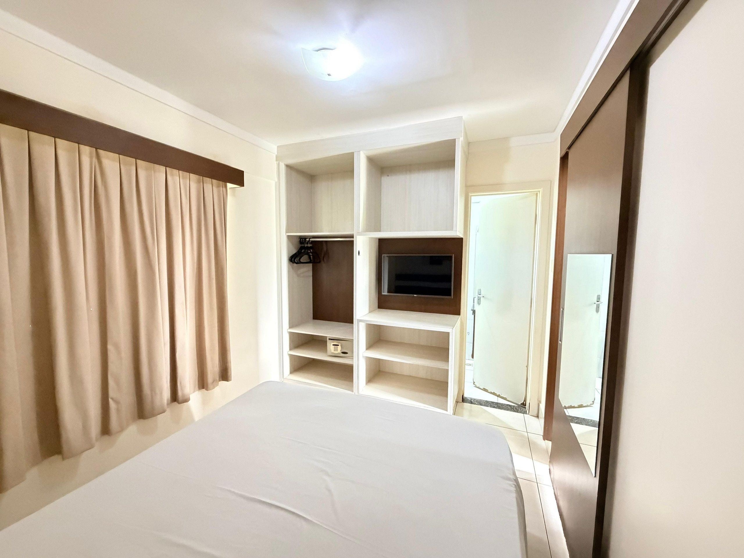 Une chambre d’hôtel avec un lit, une télévision, une armoire et un miroir.
