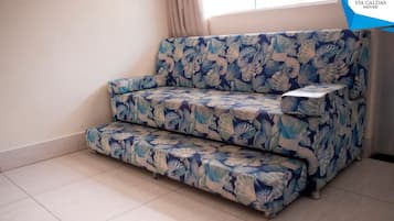 Un sofá con estampado floral en una habitación con suelo de baldosas y una ventana con cortinas.