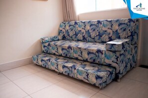Un sofá con estampado floral en una habitación con suelo de baldosas y una ventana con cortinas.