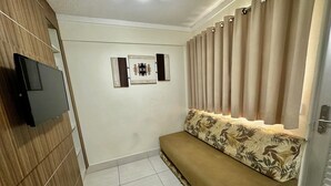 Una habitación con sofá, televisión instalada en una pared de madera y una puerta con cortinas.