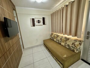 Una habitación con sofá, televisión instalada en una pared de madera y una puerta con cortinas.