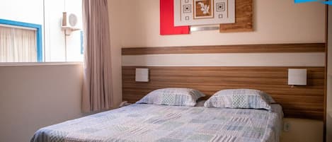A hotel room with a bed, curtains, a window, and a wall-mounted artwork.