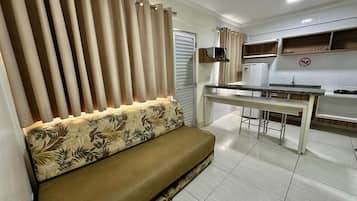 A modern living room with a sofa, a dining table, and a kitchen area with a refrigerator and cabinets.