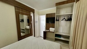 Una habitación de hotel con cama, armario con ropa colgada, televisor y espejo.