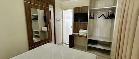 Ein Hotelzimmer mit einem Bett, einem Kleiderschrank mit Kleidung, einem Fernseher und einem Spiegel.
