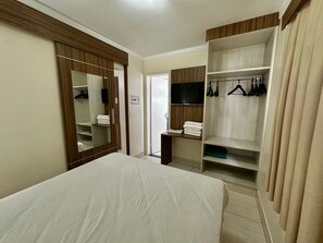 Habitació d'hotel amb un llit, un armari amb roba penjada, una televisió i un mirall.