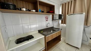 Una cucina compatta con forno a microonde, fornello e frigorifero.