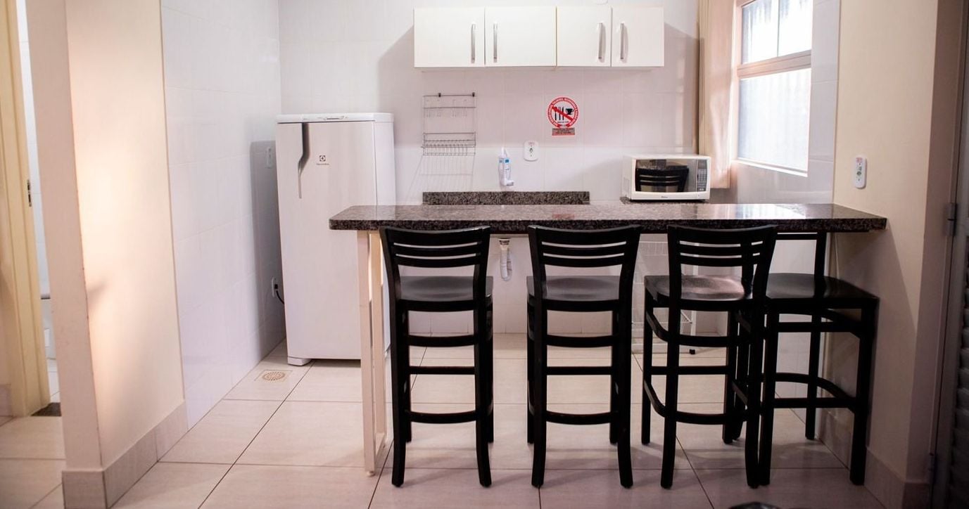 Uma cozinha compacta com geladeira, micro-ondas e uma pequena área de refeições com quatro cadeiras.