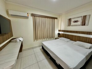 Habitación de hotel con cama, mesita de noche, televisor, ventana con cortinas y aire acondicionado instalado en la pared.