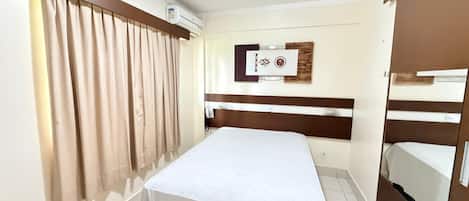 A hotel room with a bed, curtains, a wall-mounted air conditioner, a phone, and a wooden headboard.