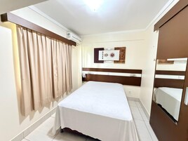 Quarto de hotel com cama, cortinas, ar condicionado fixado na parede, telefone e cabeceira de madeira.