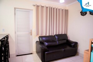 A room with a closed door, a black leather sofa, beige curtains, and a logo on the wall.