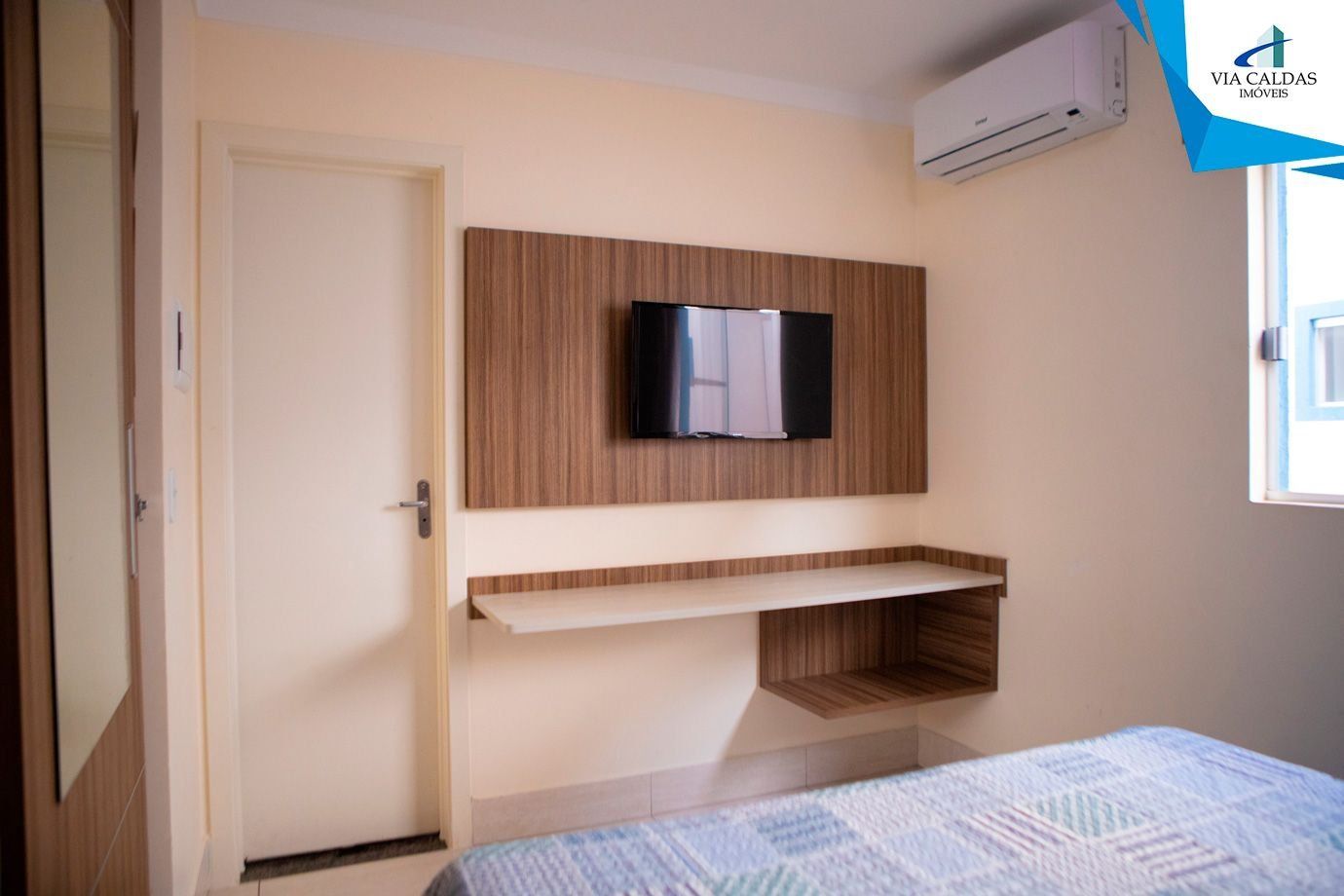 A bedroom with a bed, a mounted TV, a built-in shelf, and an air conditioning unit.