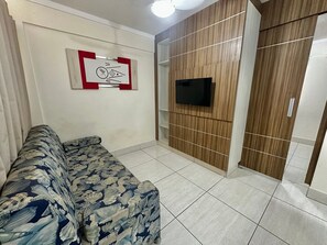 Un saló amb un sofà, un televisor penjat i una paret de panells de fusta.