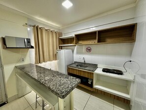 Una cocina compacta con encimera de granito, microondas integrado, refrigerador y pileta.