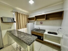 Uma cozinha compacta com bancada de granito, micro-ondas embutido, geladeira e pia.